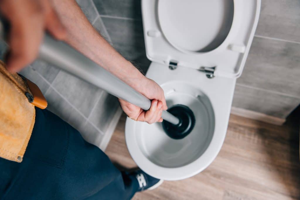 Person using a toilet plunger to unclog a toilet.