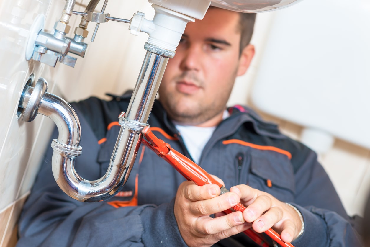 Drain clearing service, male plumber attending to a home's drain pipe.