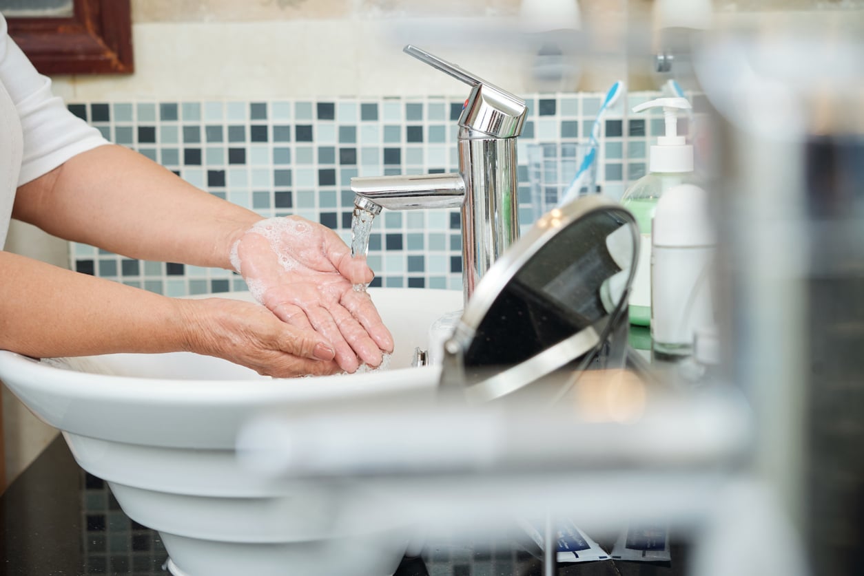 A close up of a senior woman washing her hands under the running water of her home's bathroom sink