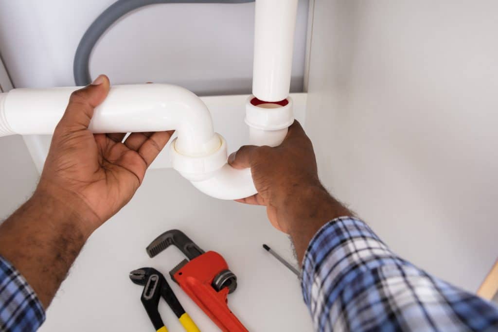 Male plumber's hands checking the water seal in a residential home's sink trap.