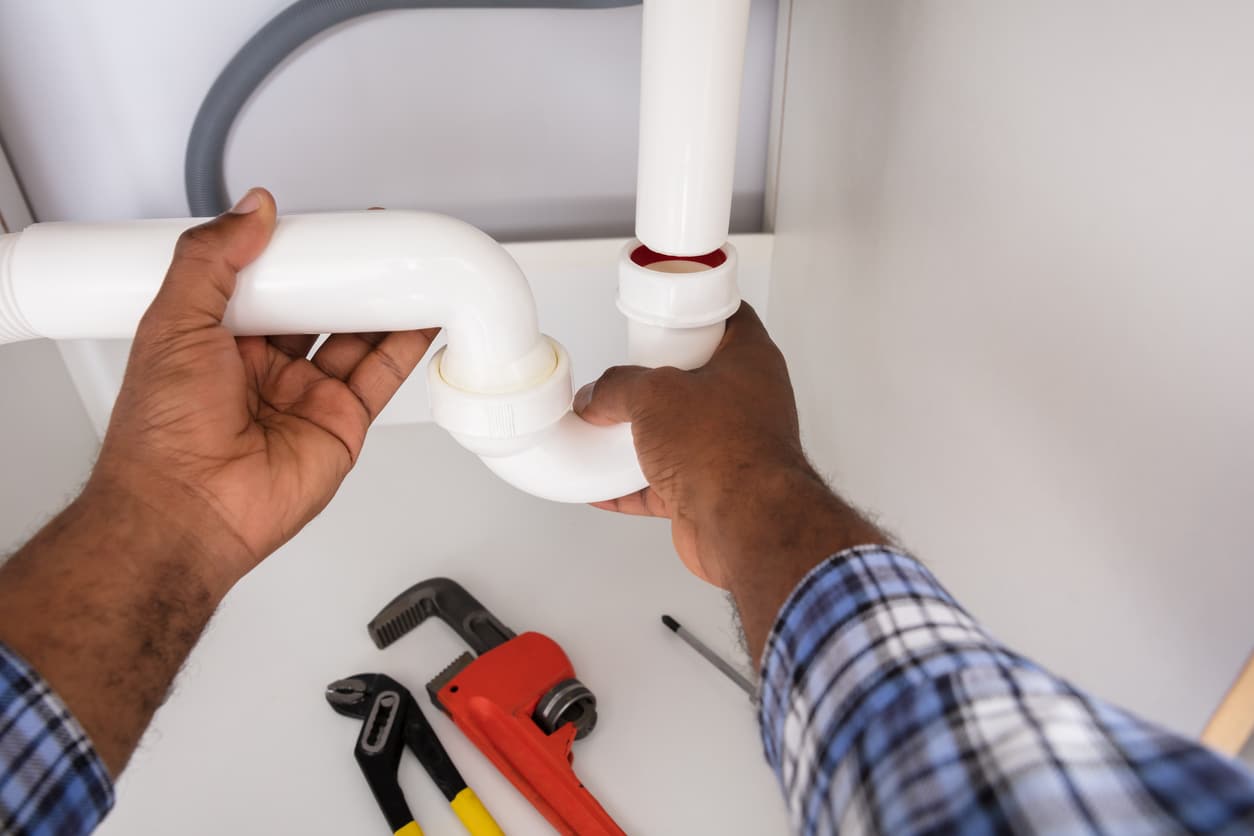 Male plumber's hands checking the water seal in a residential home's sink trap.