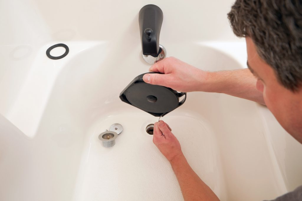 Drain maintenance concept, male plumber unclogging a bathtub drain using special tools.