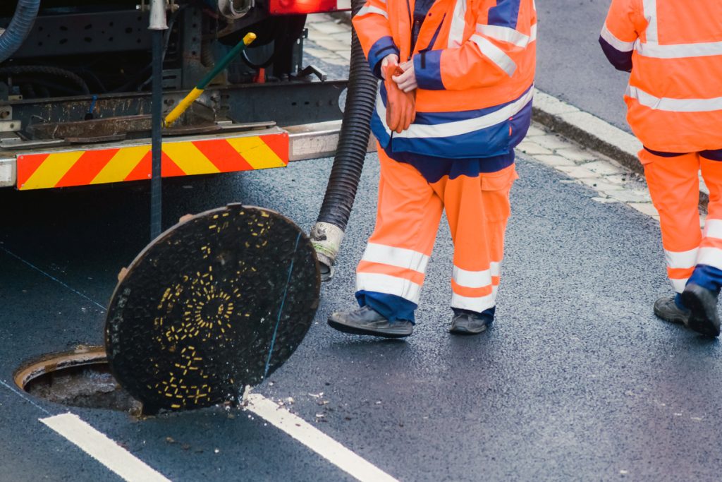 Sewer cleaning company - Two male plumbers outdoors checking a sewer line.