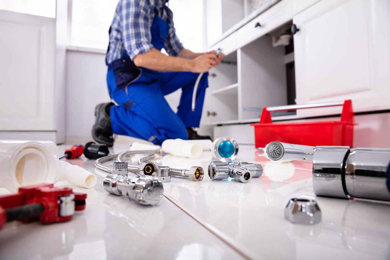 Male plumber cleaning and installing a kitchen drain system, showing different tools and equipment.