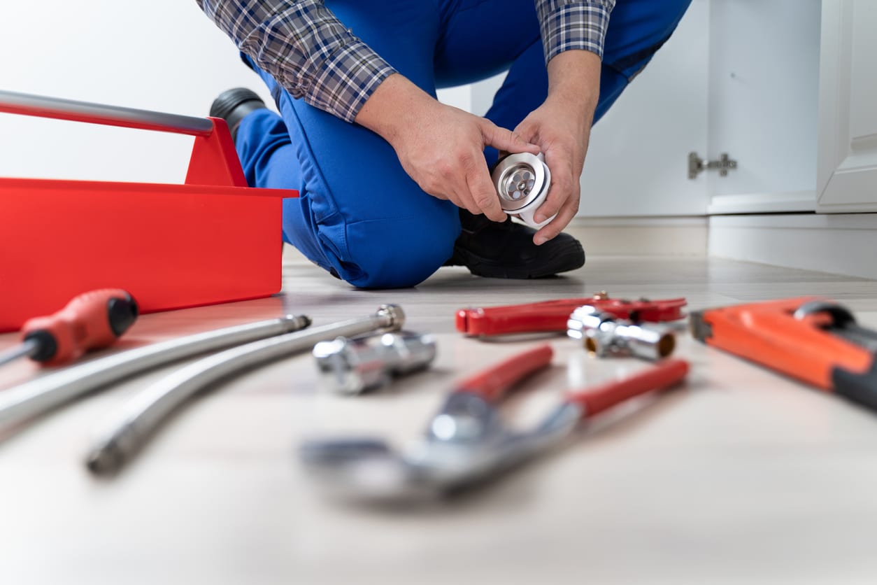 Using drain cleaning tools - male plumber unclogging a home's kitchen drain.