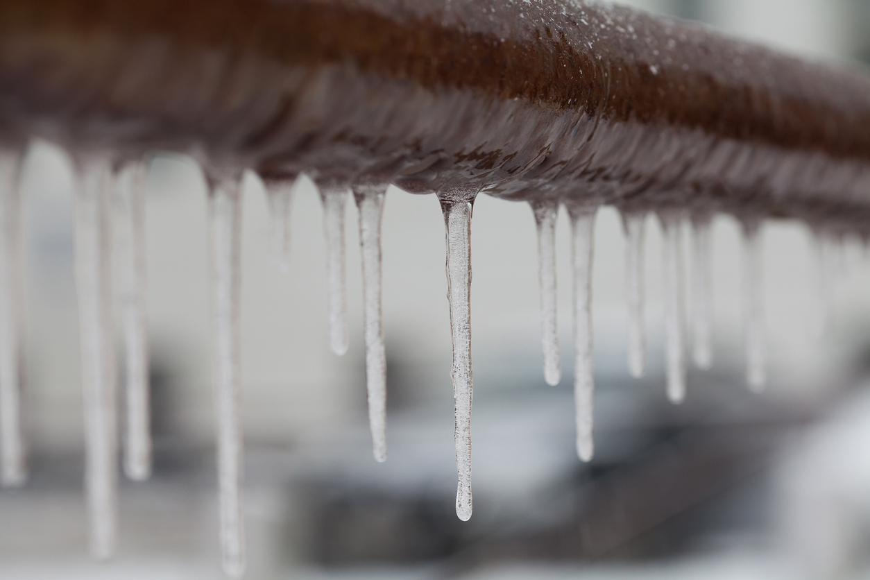 Frozen drain pipes - Icicles forming around a brown pipe during the winter season.
