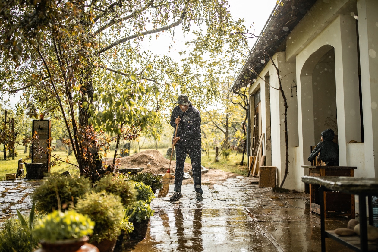 man sweeping water away from his flooded yard during a rainy day