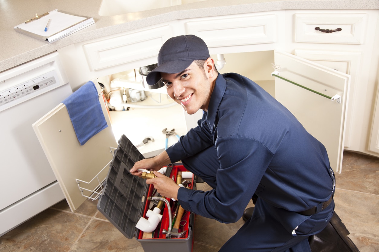 Professional male plumber providing drain cleaning and plumbing services - fixing a kitchen's clogged drains.