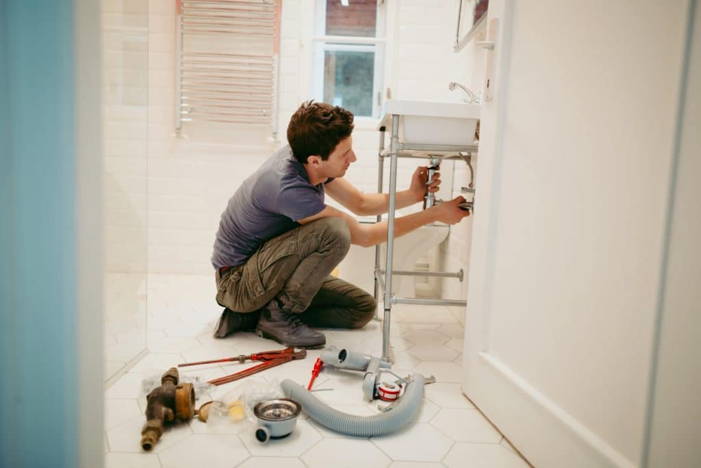 Man locating drain clog at home using different plumbing tools.