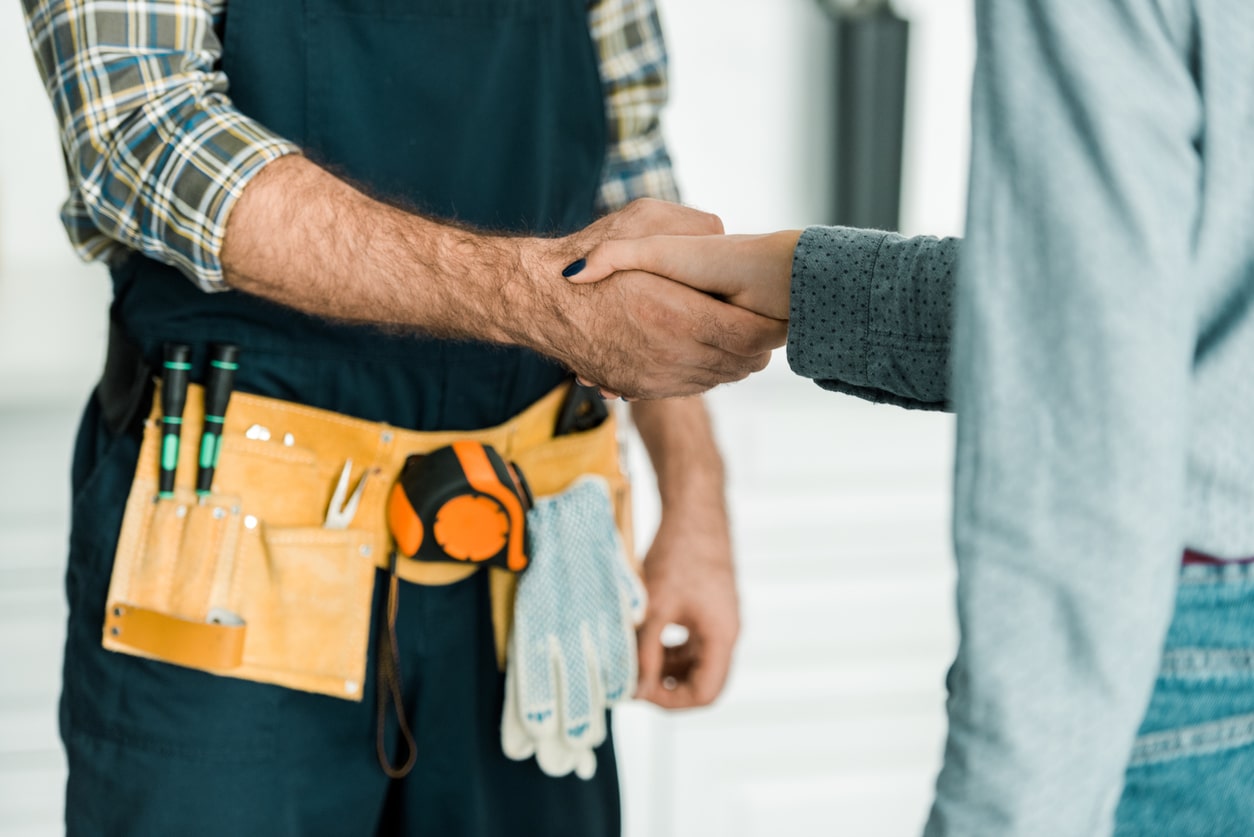 Male plumber shaking hands with a female customer in her residential home; providing drain cleaning services in NYC.