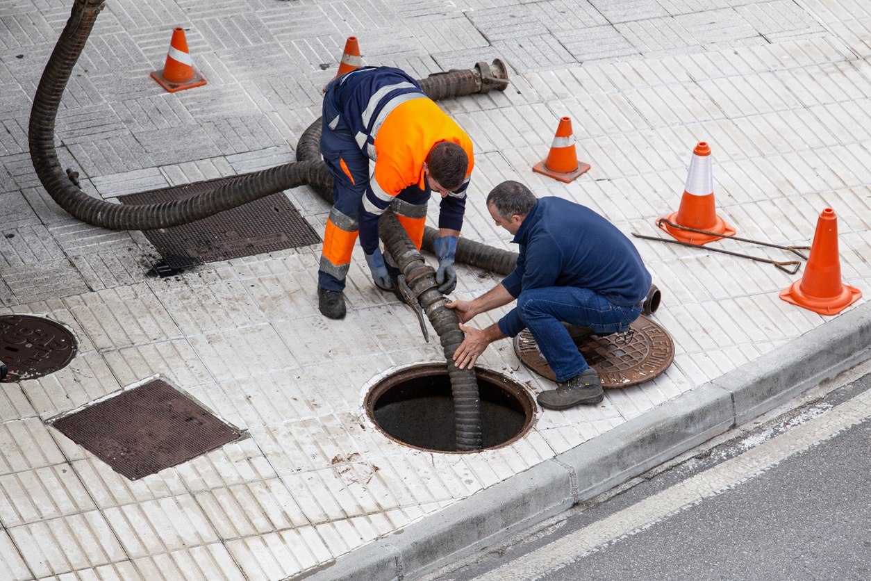 Two male plumbers in a street attending to a sewer drain issue in The Bronx.