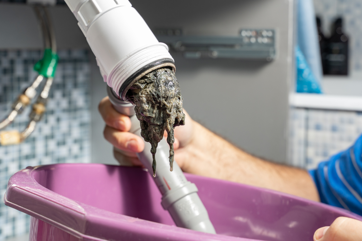 Plumber removing a large hair blockage from a bathroom pipe - causes of slow-draining sinks, in Manhattan.