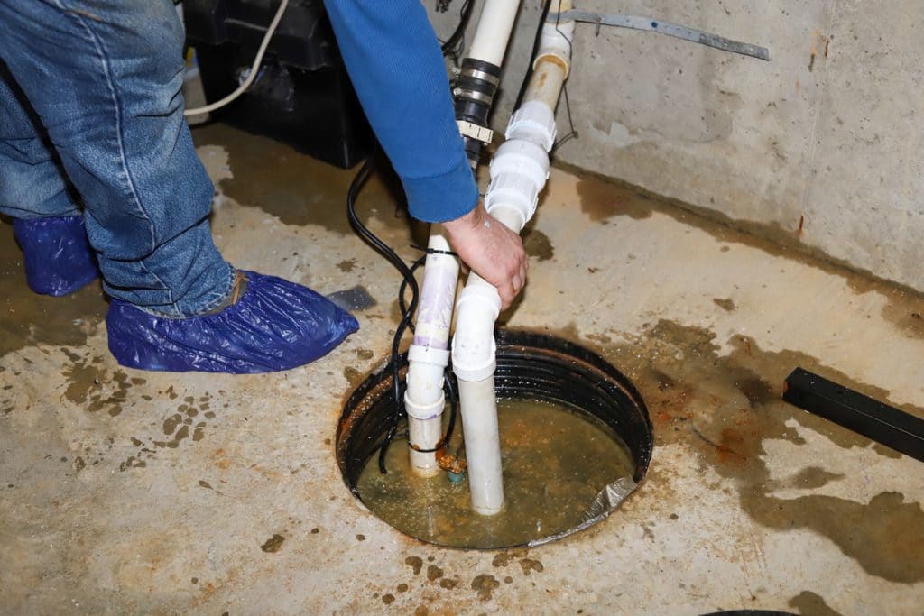 Male plumber repairing a sump pump in a flooded basement of a residential home.