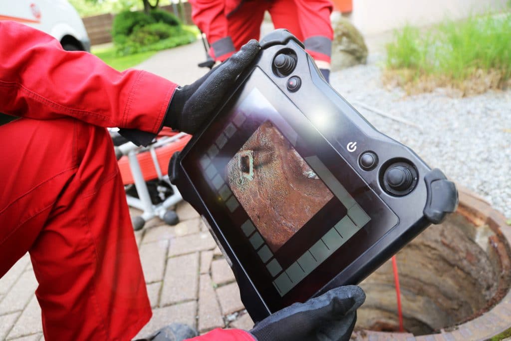 Professional plumber using HD camera and tablet to perform a home sewer video inspection.