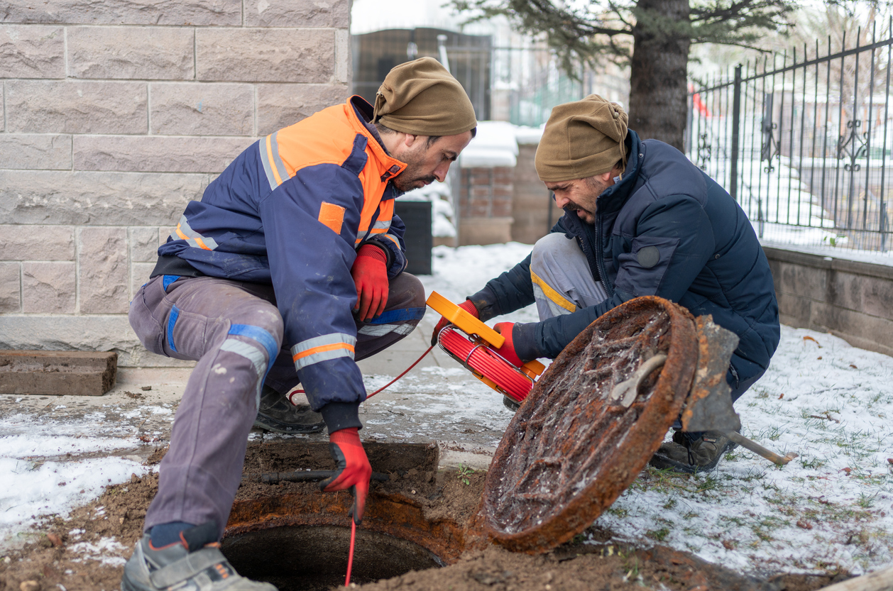 Two male plumbers conducting sewer inspection using special equipment.