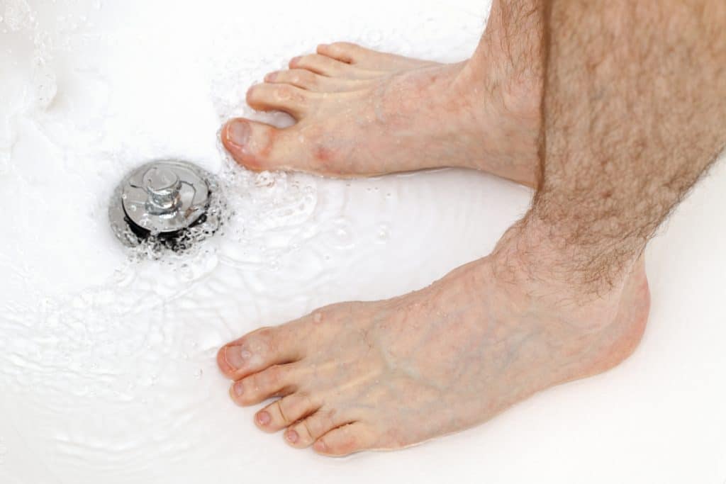 Feet of a man in a shower showing water build up near the drain
