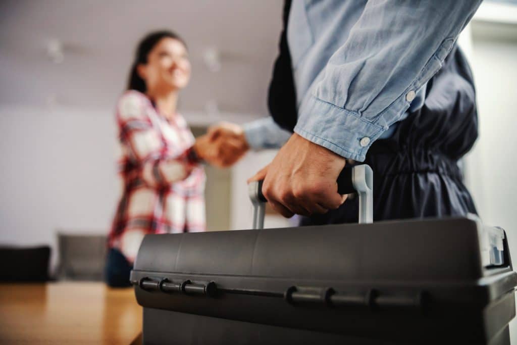 Male drain cleaning tech holding a toolbox and shaking hands with a female client at her home.