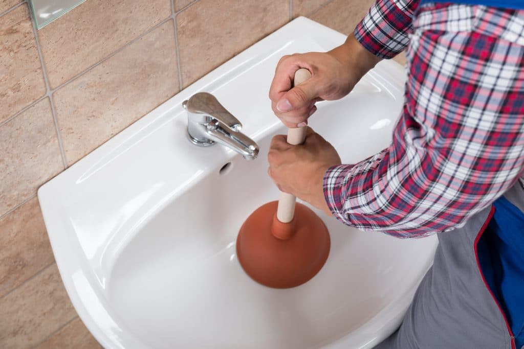 A man using a plunger on a clogged bathroom sink.