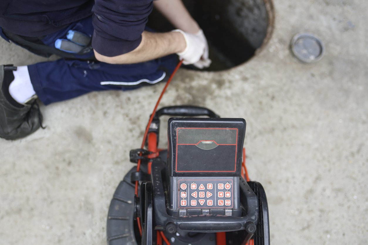 Plumbers using a video camera during a sewer line inspection - hiring drain cleaning company.